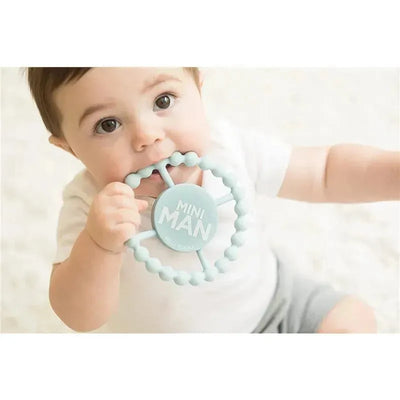 Light blue Bella Tunno Mini Man teether held by a baby, who is chewing on it, with a soft background.