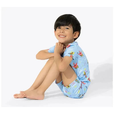 A smiling child sits cross-legged, wearing a blue short pajama set featuring Spongebob Squarepants characters.
