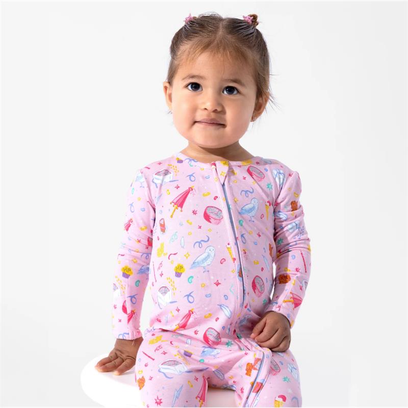 Toddler wearing a pink bamboo footie featuring colorful Harry Potter-themed patterns, smiling while seated.