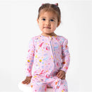 Toddler wearing a pink bamboo footie featuring colorful Harry Potter-themed patterns, smiling while seated.