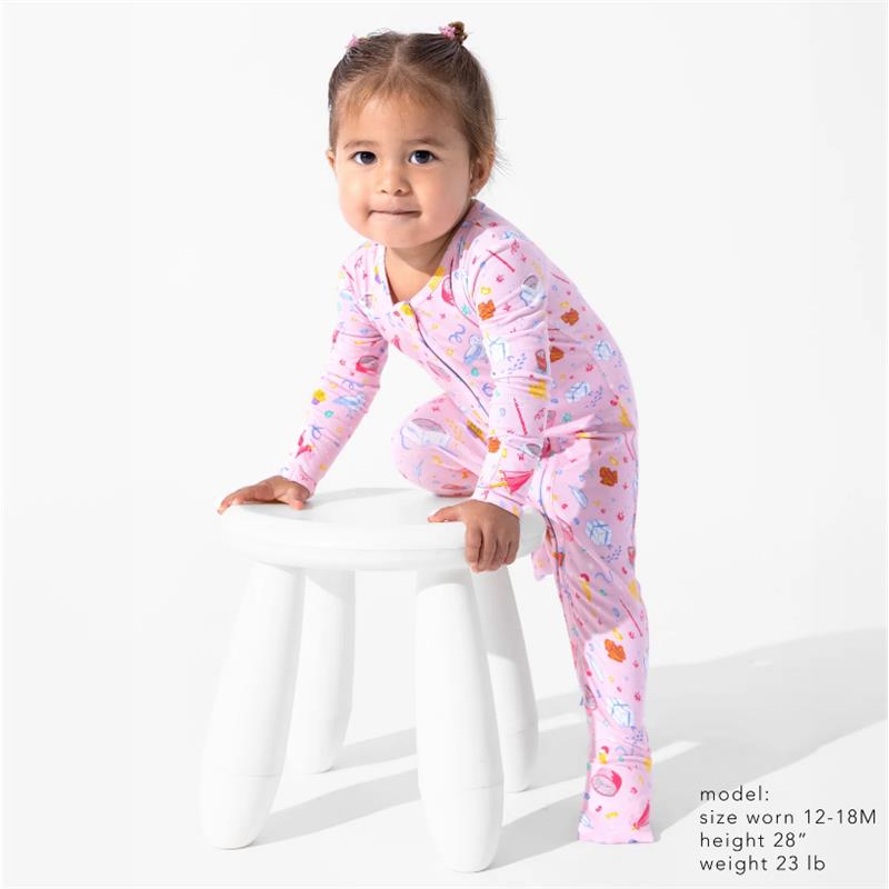 Toddler wearing a pink, patterned convertible footie with Harry Potter themes, posed on a white stool.