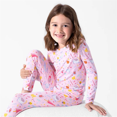 A girl wears pink Harry Potter-themed pajamas featuring colorful icons like cupcakes, wands, and stars, smiling at the camera.