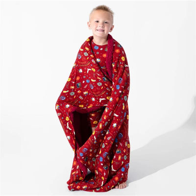 Child wrapped in a red bamboo blanket featuring Harry Potter Hogwarts Express designs, smiling with bare feet visible.