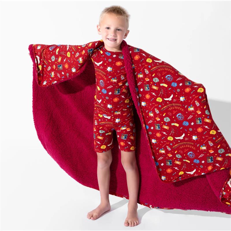 A child in a red patterned outfit holds a soft, red bamboo blanket featuring Harry Potter-themed designs.