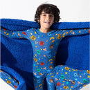 A smiling child wearing a Harry Potter-themed blue pajama set, holding a plush blue blanket featuring magical icons.