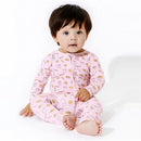 A toddler wearing pink bamboo pajamas with milk and cookie patterns, sitting and looking at the camera.