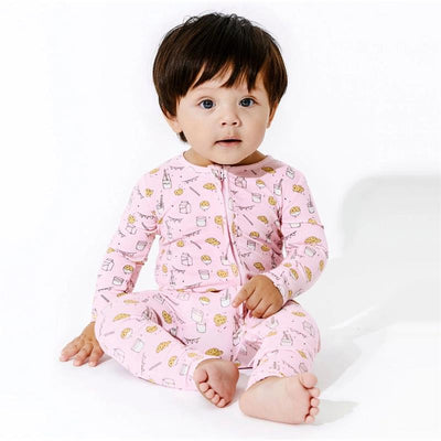 A toddler wearing pink bamboo pajamas with milk and cookie patterns, sitting and looking at the camera.