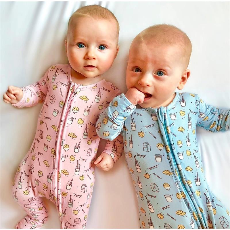 Two babies in bamboo pajamas, one pink with milk and cookies patterns, one blue with similar designs, on a white surface.
