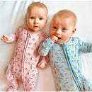 Two babies in bamboo pajamas, one pink with milk and cookies patterns, one blue with similar designs, on a white surface.