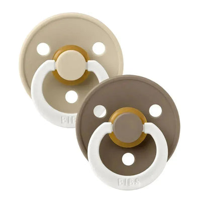 Two BIBS rubber baby pacifiers in Vanilla and Dark Oak colors, designed for infants 0-6 months, featuring a round shield and handle.