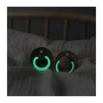 Rubber baby pacifiers in dark oak and glowing vanilla, resting on a soft surface, designed for 0-6 months.