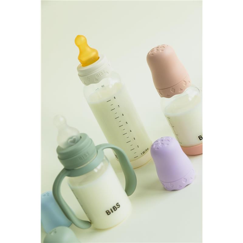 Baby blue Bibs baby bottle handle and various baby bottles with silicone lids in soft colors, filled with milk.