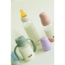Baby blue Bibs baby bottle handle and various baby bottles with silicone lids in soft colors, filled with milk.