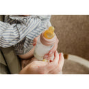 Baby blue plastic bottle with latex nipple, held by a caregiver, containing liquid, against a neutral background.