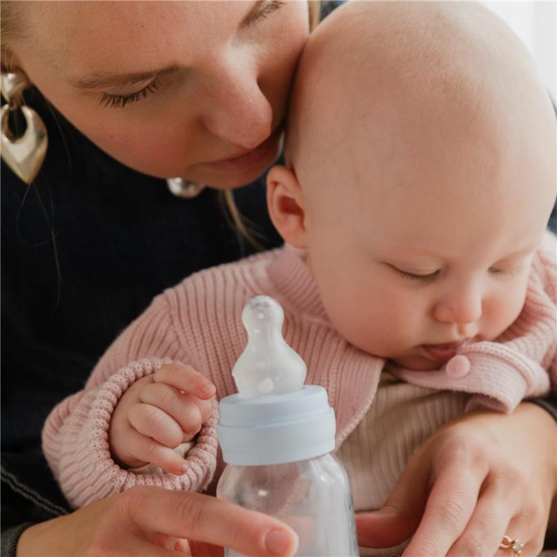 Baby holding a Bibs 270ml plastic bottle with silicone nipple, with an adult leaning in closely.