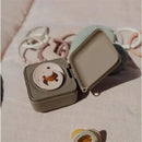BIBS petrol-colored pacifier box open, showcasing a pacifier inside, with additional pacifiers nearby on a soft surface.