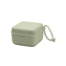 Square sage green pacifier box with a lid and attached strap, designed for storing pacifiers safely.