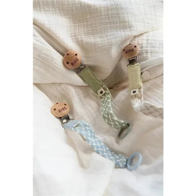 Three Bibs pacifier clips in Dark Oak and Vanilla colors, featuring wooden clips and fabric straps with various patterns.