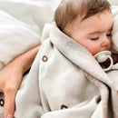 A sleeping baby wrapped in a cream-colored swaddle blanket with a soft texture, featuring subtle circular patterns.