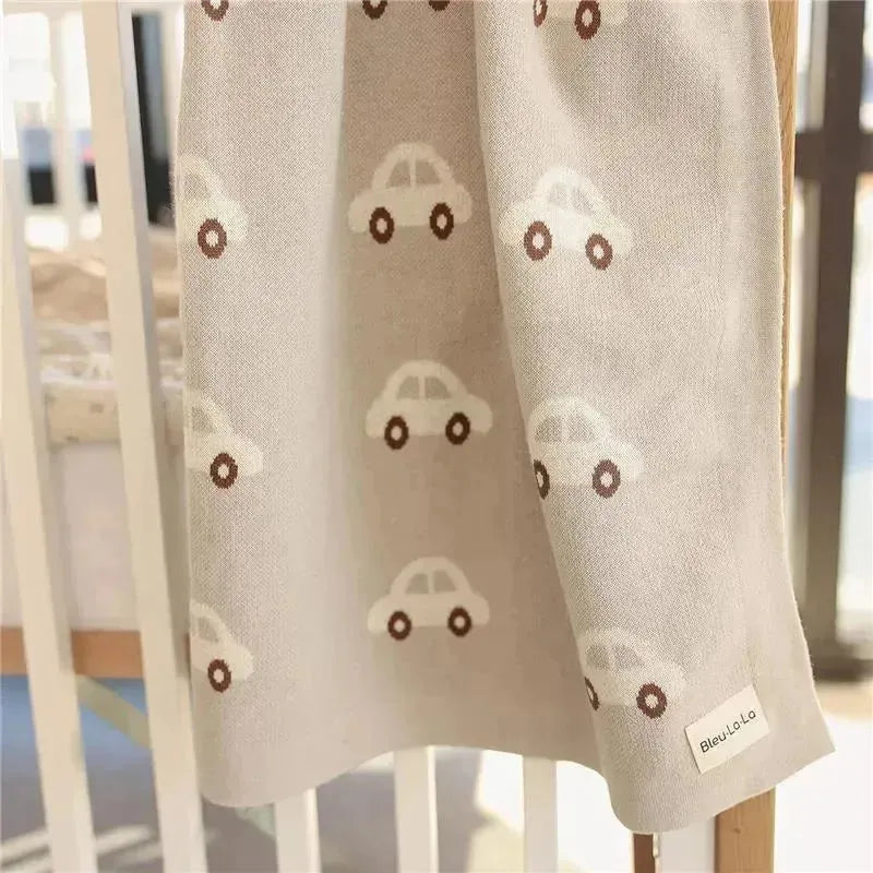 100% luxury cotton swaddle blanket in cream color, featuring small car patterns and a Bleu La La label.