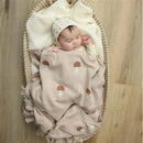 Luxury cotton swaddle blanket in mushroom camel pattern, with a sleeping baby swaddled inside, in a cozy bassinet.
