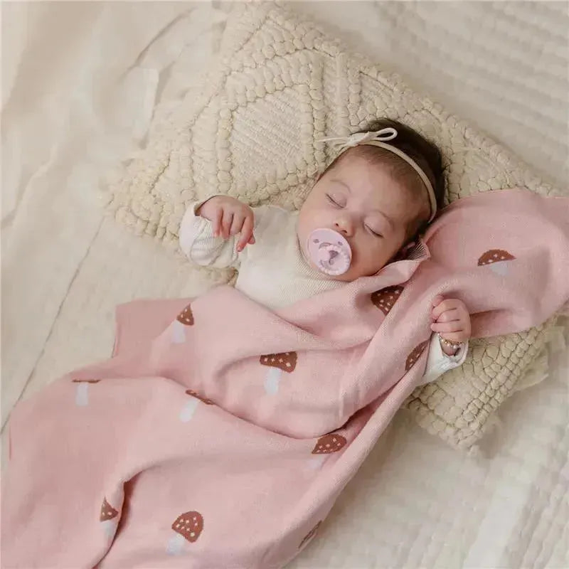Baby peacefully sleeping on a textured pillow, wrapped in a pink mushroom-patterned swaddle blanket.