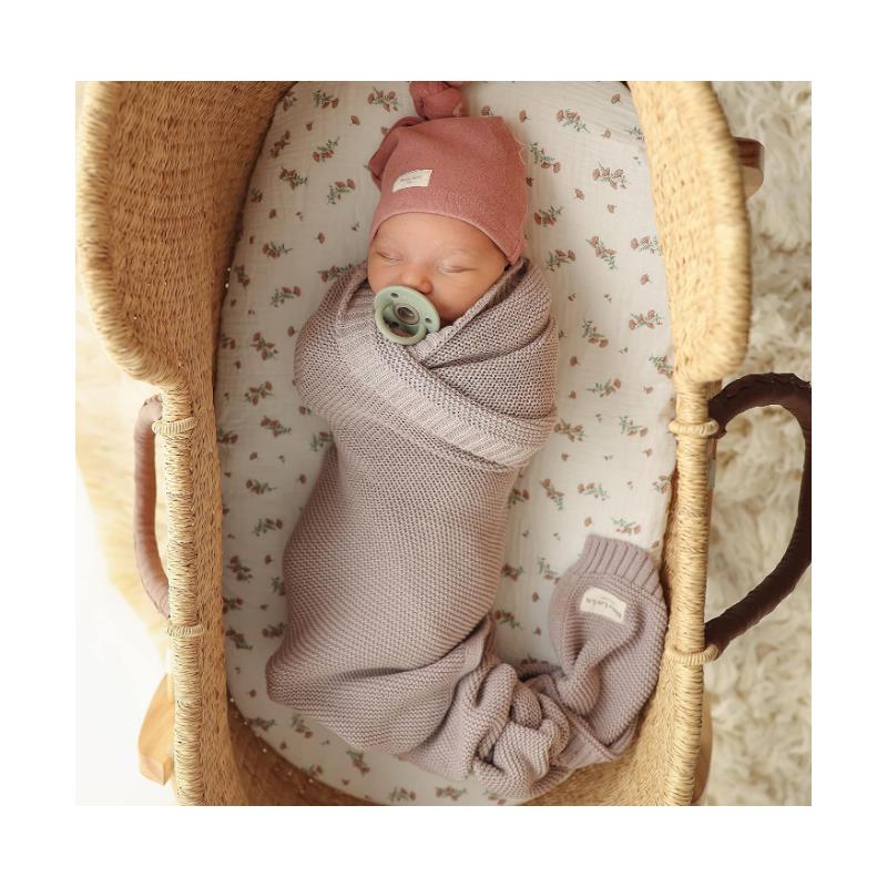Luxury cotton swaddle blanket in sheep ivory wraps a sleeping baby with a pacifier, nestled in a woven bassinet.