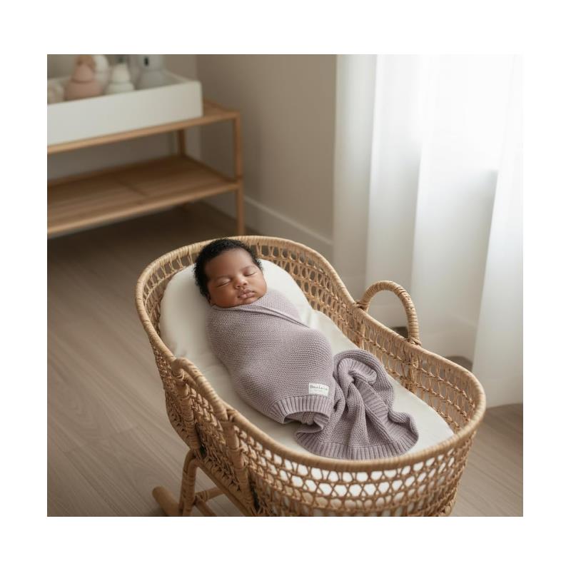 Luxury cotton swaddle blanket in sheep ivory wraps a peacefully sleeping baby in a cozy bassinet.