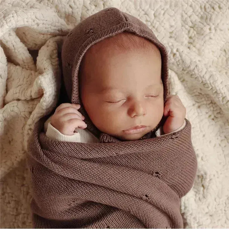Luxury organic blanket and bonnet hat set in blue, with a sleeping baby swaddled in the blanket.