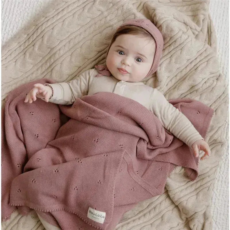 Luxury organic cotton blanket and bonnet hat set in blue, draped over a baby lying on a textured surface.