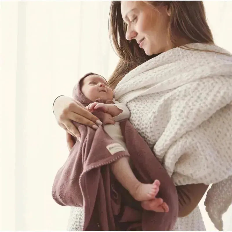 Luxury organic cotton blanket and bonnet hat set in blue, wrapped around a baby held by a smiling woman.