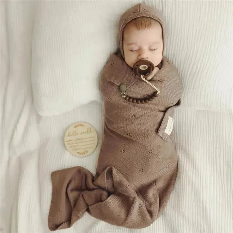 Luxury organic blanket and bonnet hat set in blue, featuring a swaddled baby with a pacifier on a textured white surface.