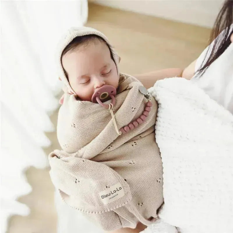 Organic cotton luxury blanket and bonnet hat set in blue with a sleeping baby wrapped in the blanket, pacifier included.