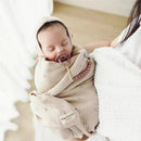 Organic cotton luxury blanket and bonnet hat set in blue with a sleeping baby wrapped in the blanket, pacifier included.