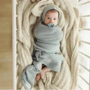 Organic cotton luxury blanket and bonnet hat set in blue, featuring a wrapped baby with a pacifier on a textured blanket.