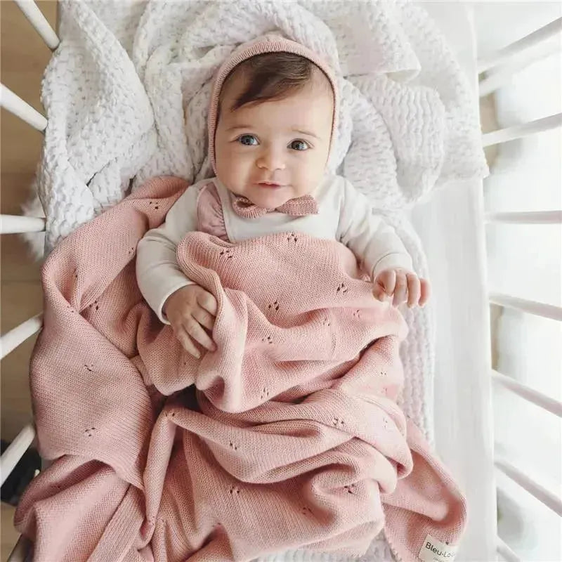 Organic cotton pointelle baby blanket in ballet slipper color, draped around a smiling baby in a crib.