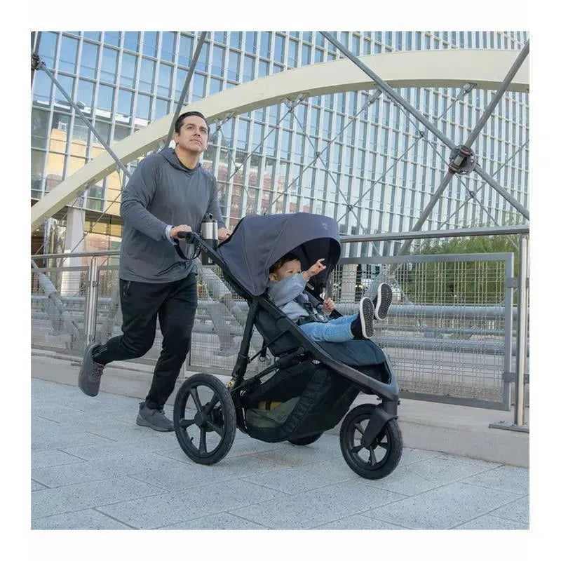 Jogger pushing the BOB Wayfinder Jogging Stroller, Storm, with a child pointing forward, in an urban setting.