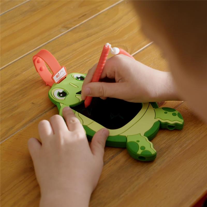 Child drawing on a green turtle-shaped doodle board with a red stylus on a wooden surface.