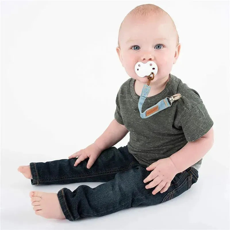 Toddler wearing a gray shirt and denim jeans, sitting with a pacifier attached to a denim strap.