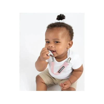 Baby wearing a white shirt and beige shorts, holding a pacifier clip with pink arrows, smiling at the camera.