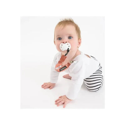 Baby with a pacifier attached to a Booginhead clip, wearing a white long-sleeve shirt and striped pants.