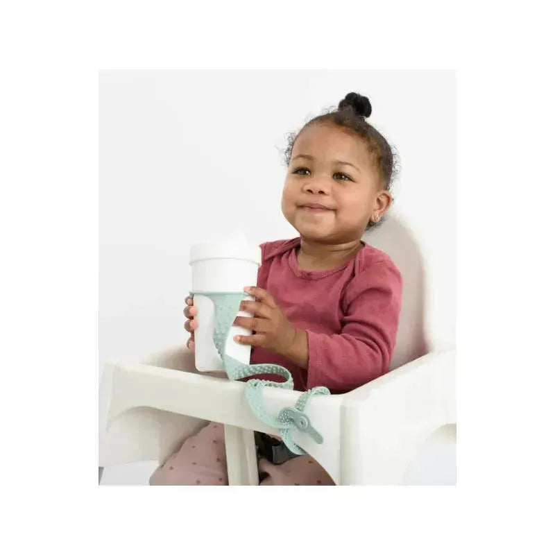 Child in a high chair holding a green sage Booginhead Silicone Sippigrip Cup, smiling while grasping the attached toy holder.
