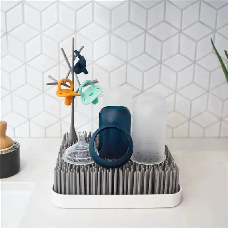 Boon GRASS Countertop Drying Rack in grey displaying various baby bottles and accessories on drying spikes.