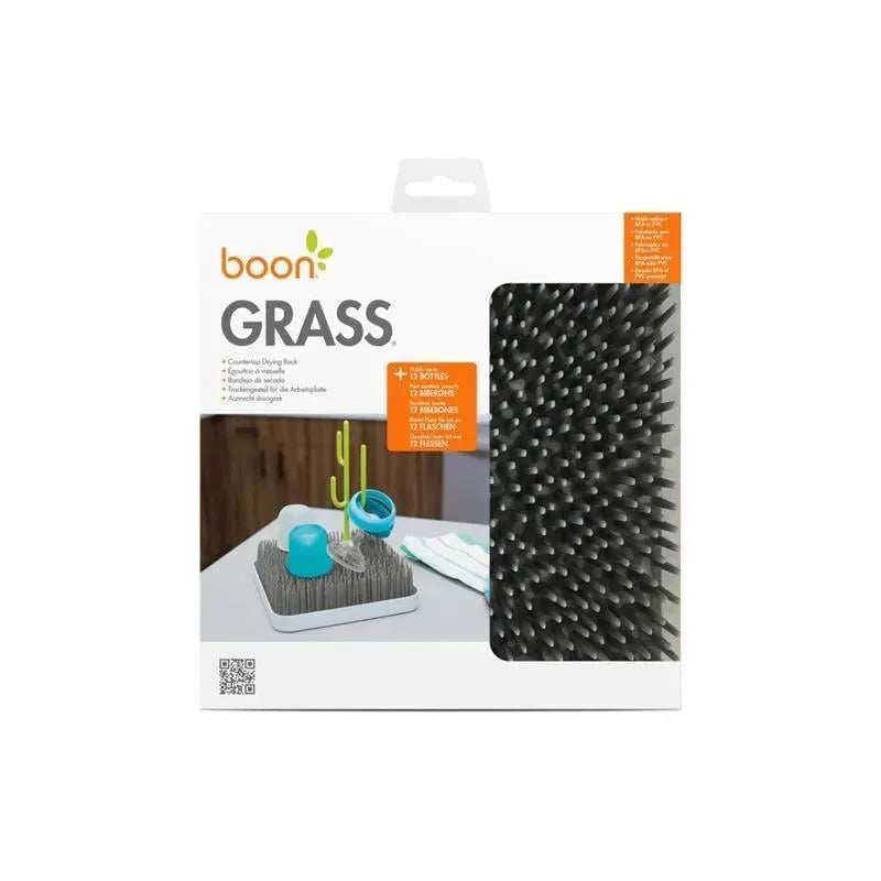 Boon GRASS countertop drying rack in grey, featuring leaf-like spikes and blue bottle accessories on a tabletop.