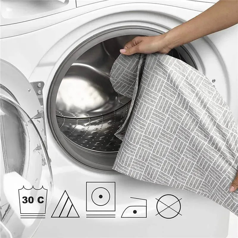 A hand places a gray basket weave-patterned Boppy Cuddle Pregnancy Pillow into a washing machine, with care instructions visible.