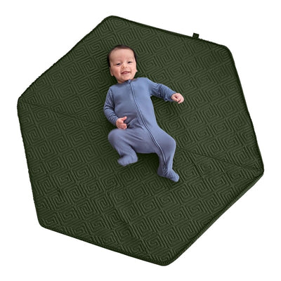 Baby in a blue onesie lying on a moss-green hexagonal Boppy foam play mat with a textured pattern.