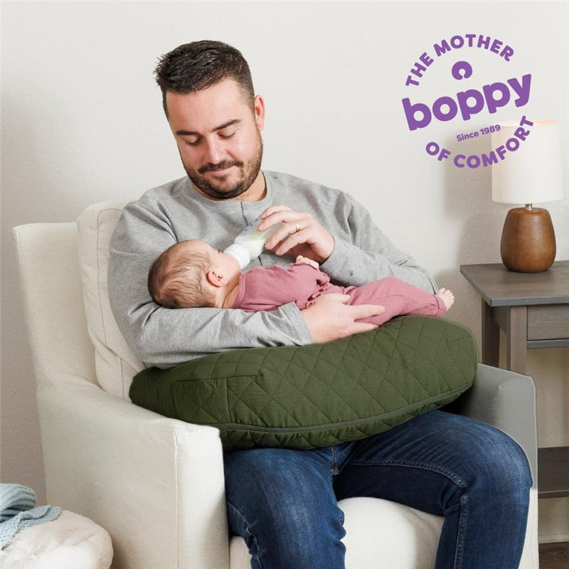 A man holds a baby in a Boppy Nursing Pillow Luxe in moss green while feeding with a bottle, smiling gently.