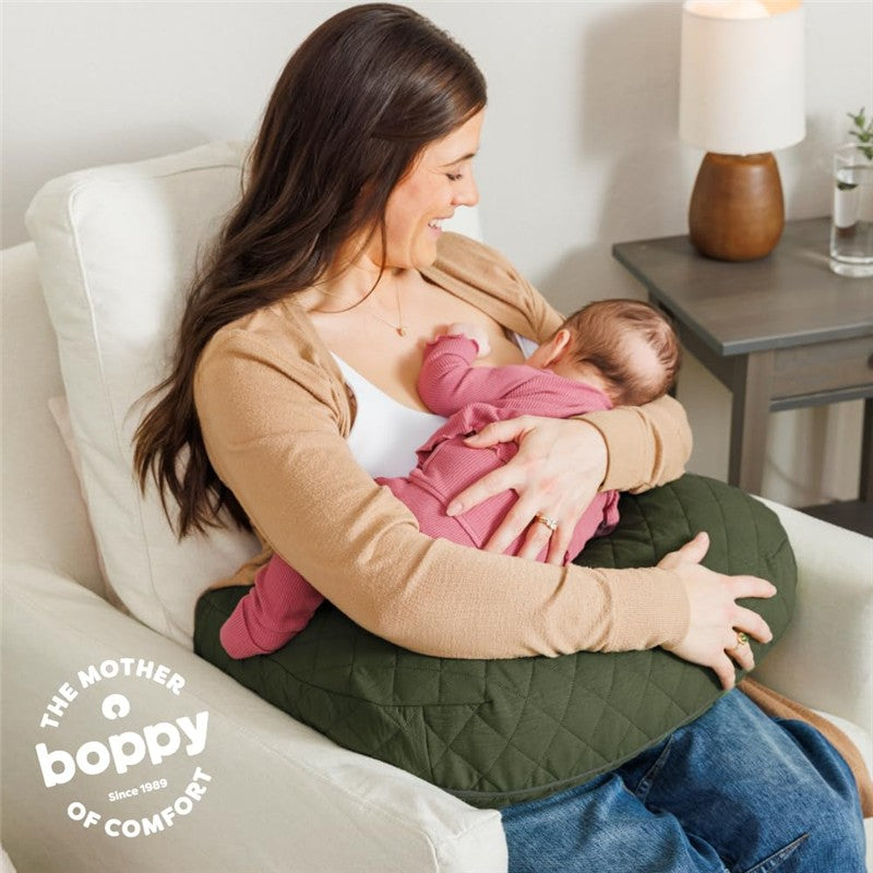 A mother uses a Boppy Nursing Pillow Luxe in moss quilted fabric while breastfeeding her baby, both relaxed on a couch.