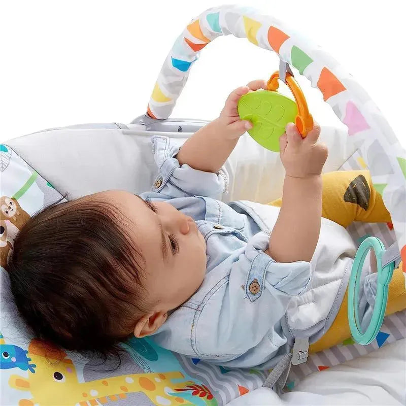 Baby in a Bright Starts bouncer playing with a green toy. The seat features colorful animal patterns and a safety harness.