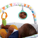 Baby in a Bright Starts bouncer, reaching for colorful hanging toys and looking at their reflection in a mirror.